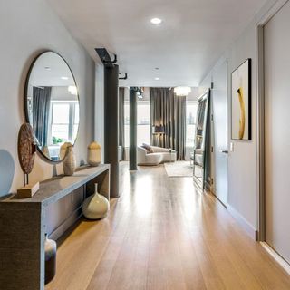 hallway with wooden floor and round mirror and white wall