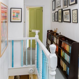 Landing with dark brown bookcases along one wall containing a colourful assortment of books, a lime green painted door and staircase rail painted in various shades of blue and white