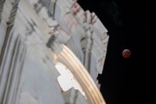 total lunar eclipse shows a red moon on the right and a large building on the left.