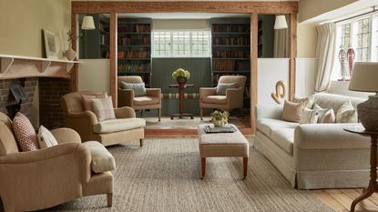 a cozy cottage living room in hampstead with a neutral rug, inglenook fireplace, a beamed nook area with dark green bookcases and layered furniture