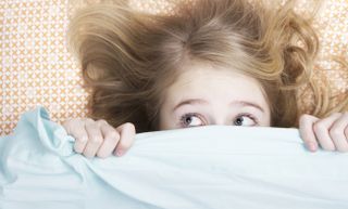Child or teen hiding under covers in bed