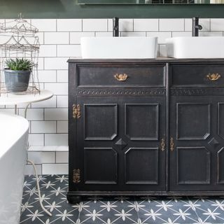 A bathroom with patterned floor tiles and an antique black cupboard for under-sink storage