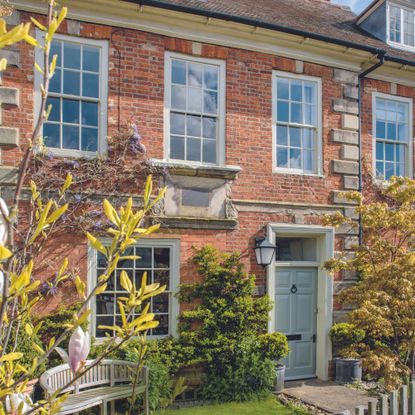 A red brick house with a a wooden front door and a magnolia tree outside it