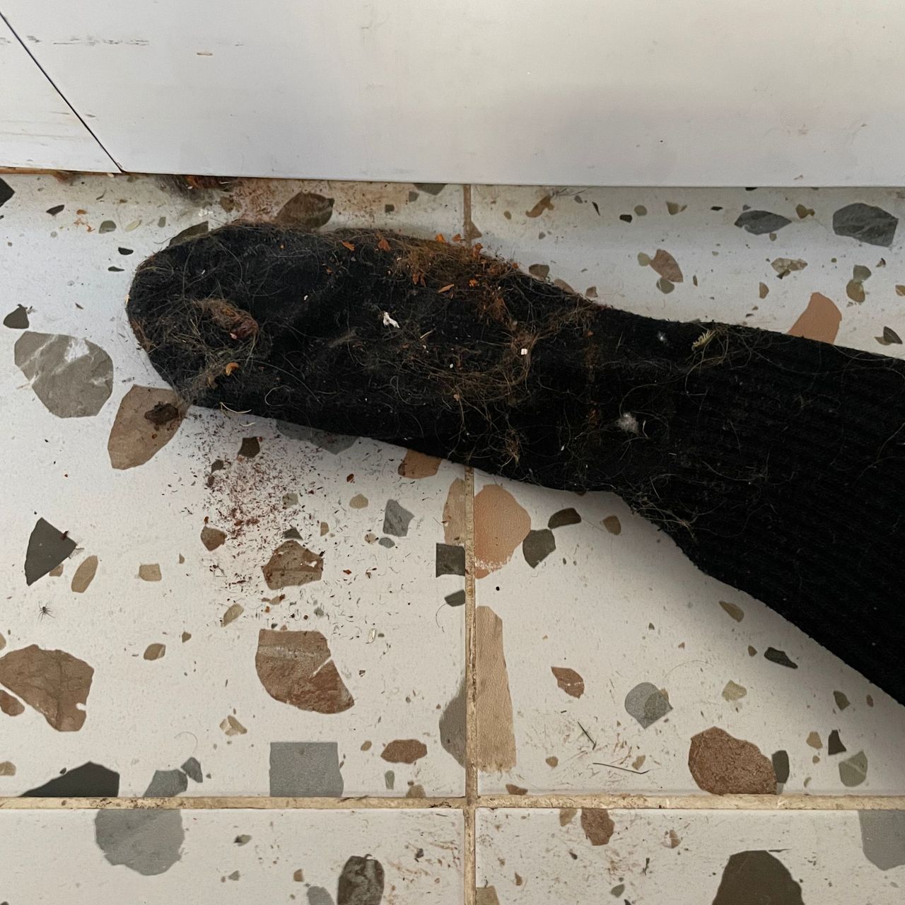 Wire hanger with a sock over it, pulling dirt out from underneath a washing machine