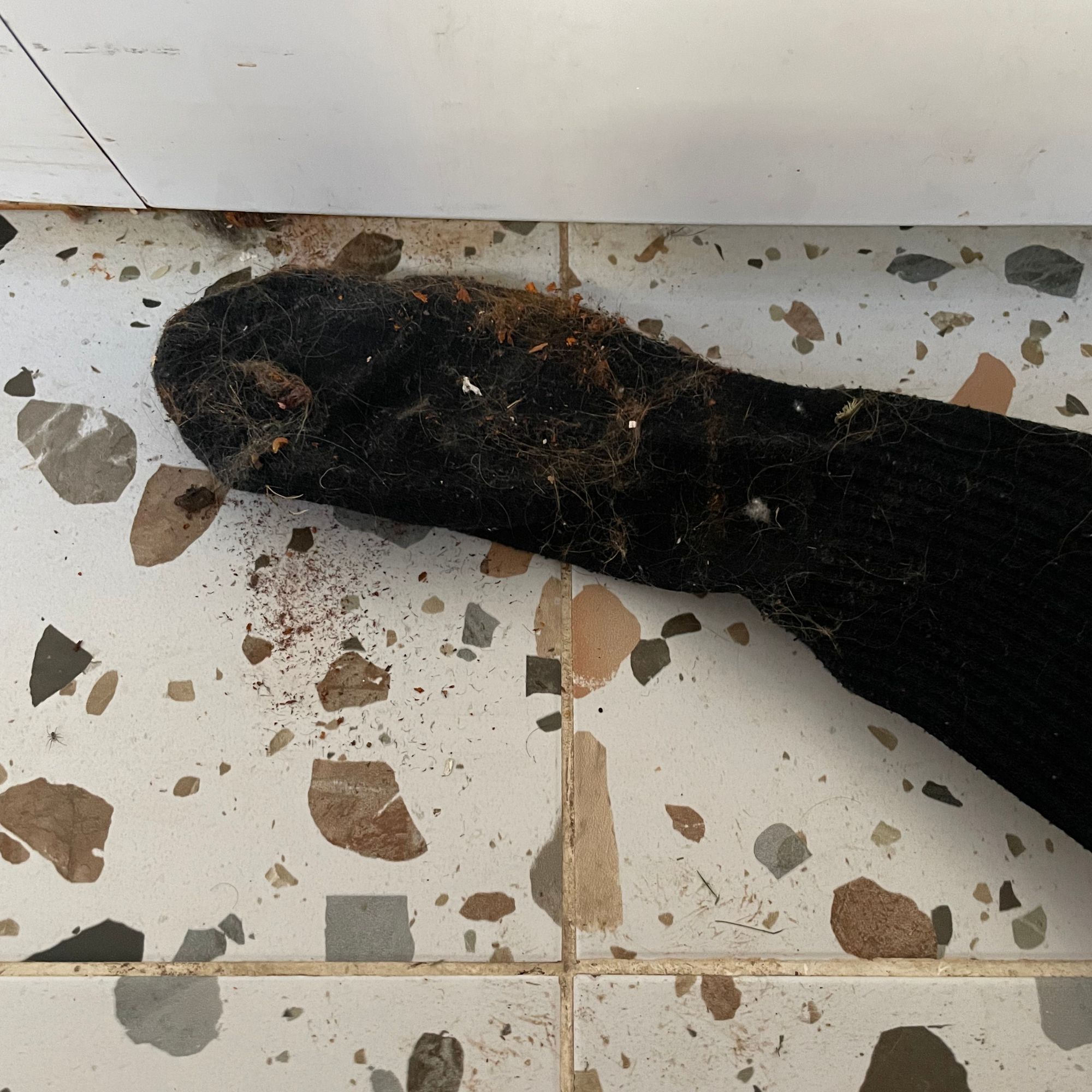 Wire hanger with a sock over it, pulling dirt out from underneath a washing machine
