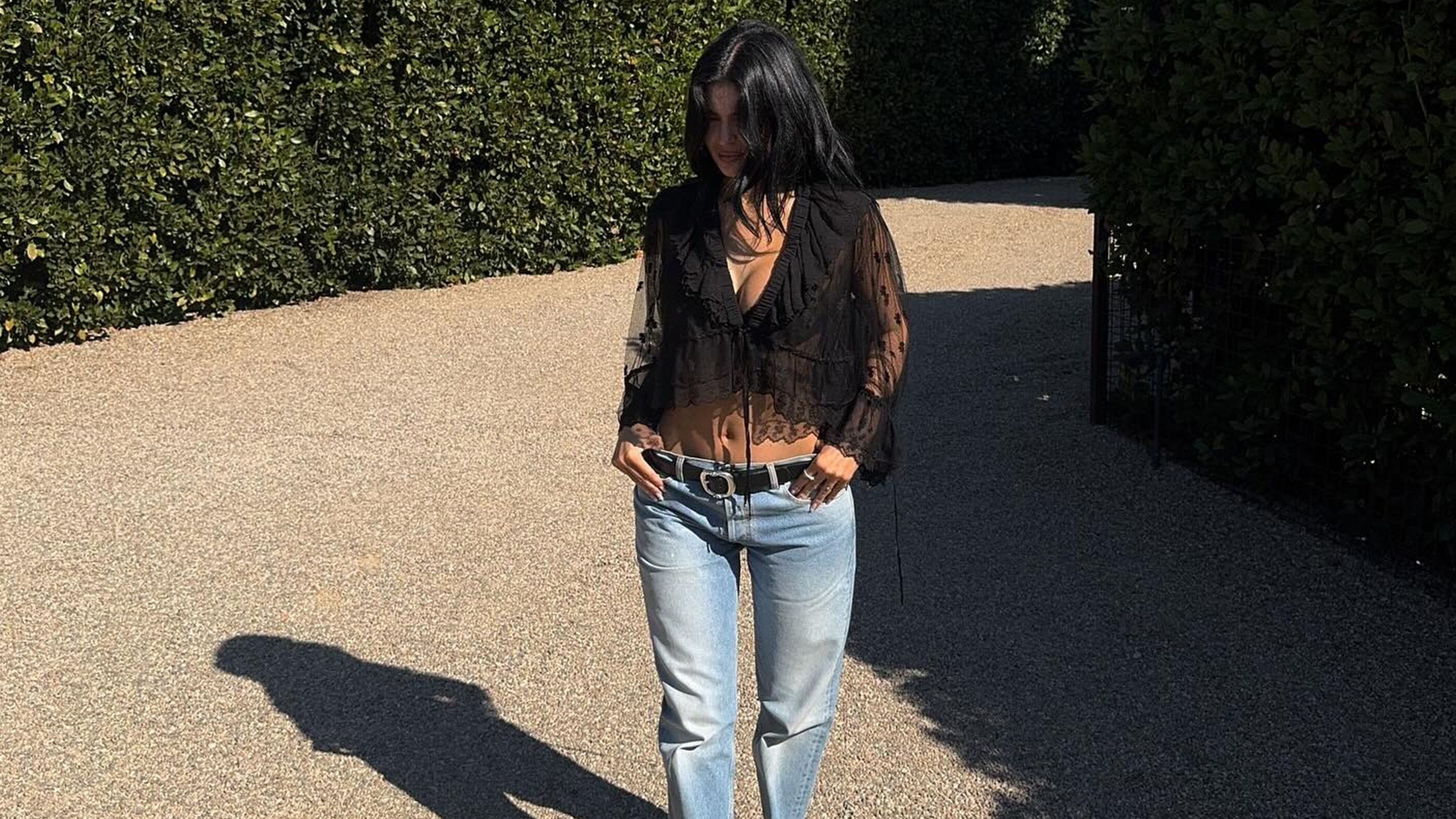 Kylie wears a black lace blouse, black leather belt, and low-rise jeans.