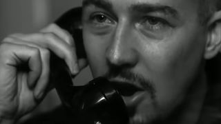 A close up of Edward Norton on a phone behind glass