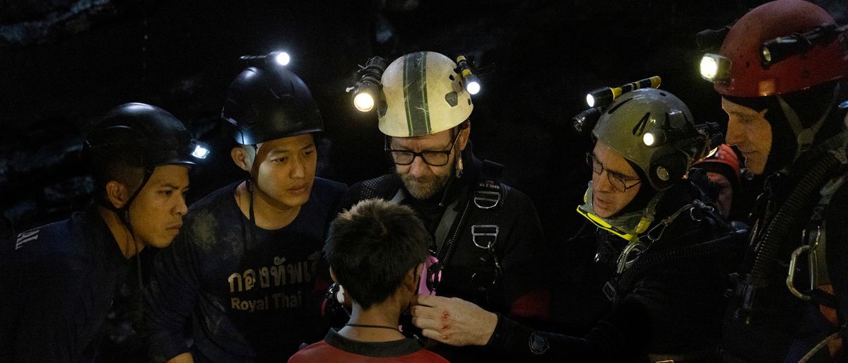 Thira ‘Aum’ Chutikul, Popetorn ‘Two’ Soonthornyanakij, Joel Edgerton, Colin Farrell, and Viggo Mortenson standing in front of kids in a cave in Thirteen Lives.