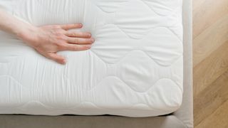 A person places their hand on top of a white mattress to check for sagging