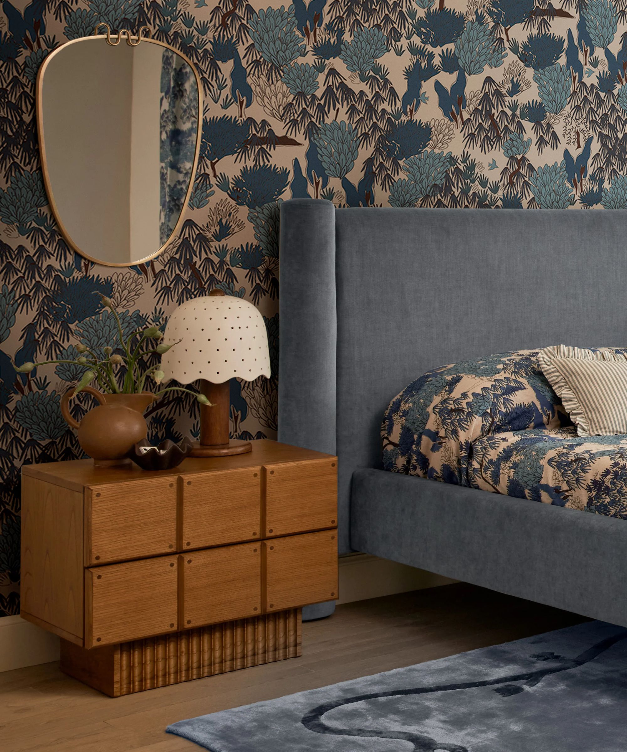 blue pattern drenched bedroom with matching blue floral printed wallpaper, drapes and bed linens with a large blue rug, blue velvet upholstered bed and wooden nightstands