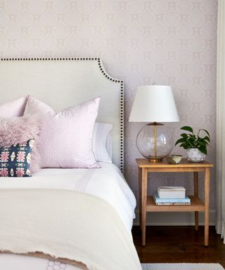 A bedroom with lavender wallpaper, a white bed with lavender pillows, and a wooden nightstand