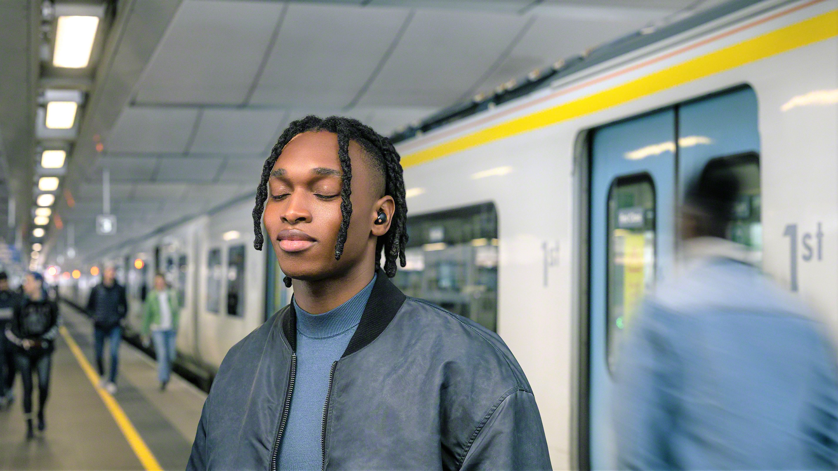 Sony WF-1000XM5 image showing young man wearing earbuds on an underground station platform