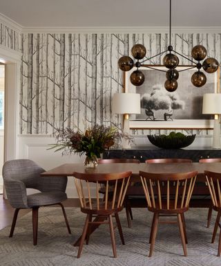 A dining room with tree-inspired wallpaper, wooden dining chairs, and a sculptural light fixture