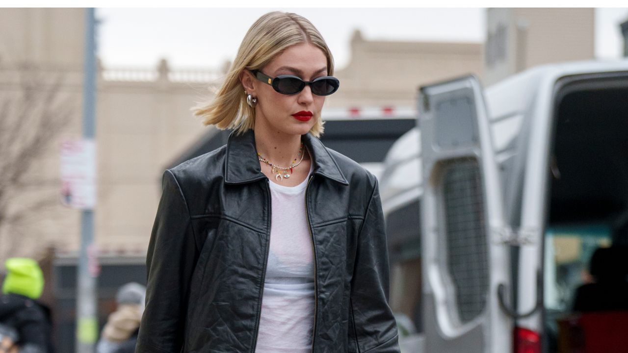 Gigi Hadid crossing the street in a white tee shirt and leather jacket.