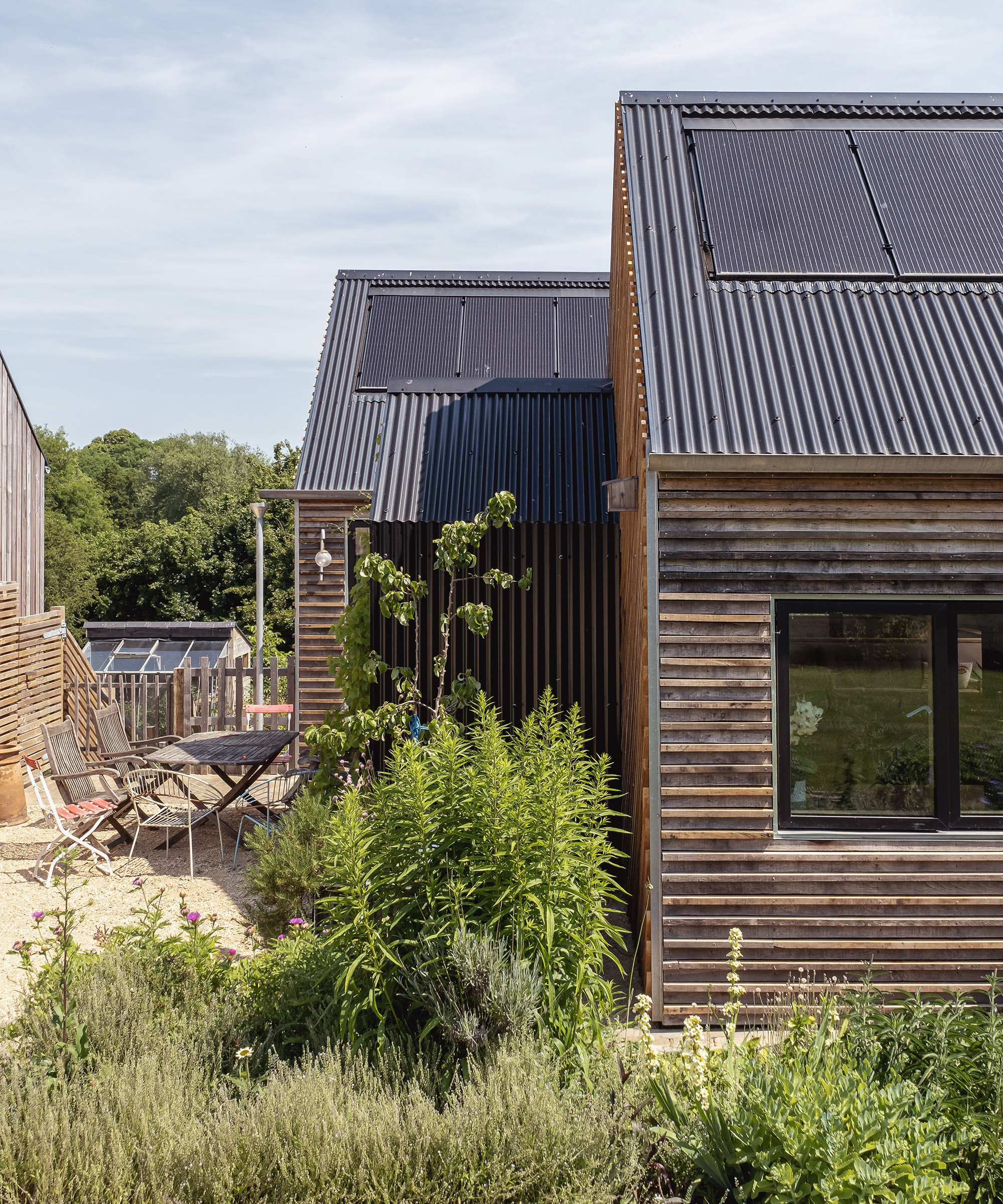 Two single storey buildings with pitched roofs and solar panels next to each other in a self build plot