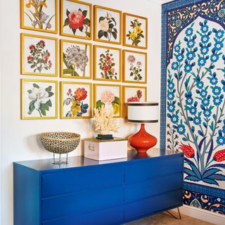 Colourful bedroom with blue sideboard for storage and a gallery wall of botanical art prints