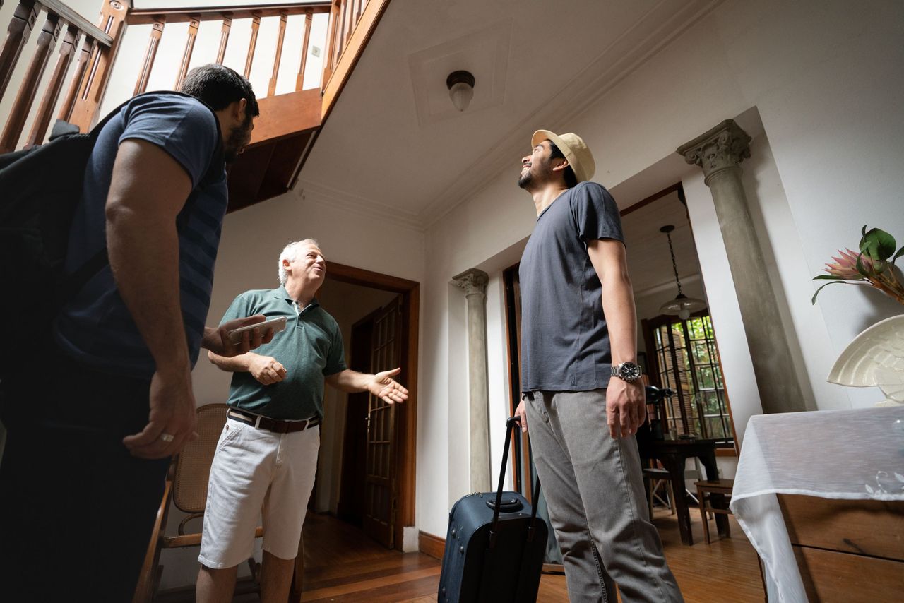 A homeowner talks to two travelers who are renting out his house. 