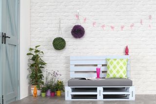 Pallet garden seating with outdoor cushions and propped against a whitewashed wall