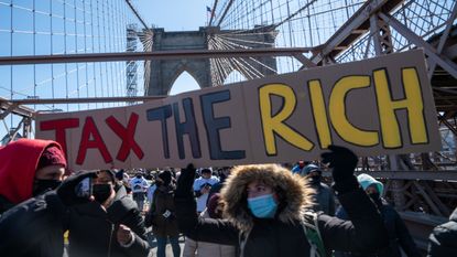 picture of protester on bridge holding large sign saying "Tax the Rich"