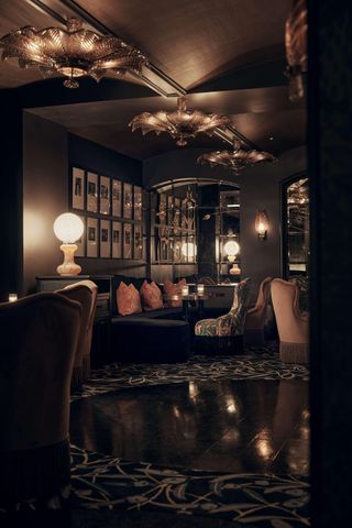 An Art Deco-inspired subterranean cocktail bar is adorned with Murano glass, flower-shaped chandeliers, spherical lighting, ornate textiles, and framed artworks, all immersed in a warmly lit atmosphere.