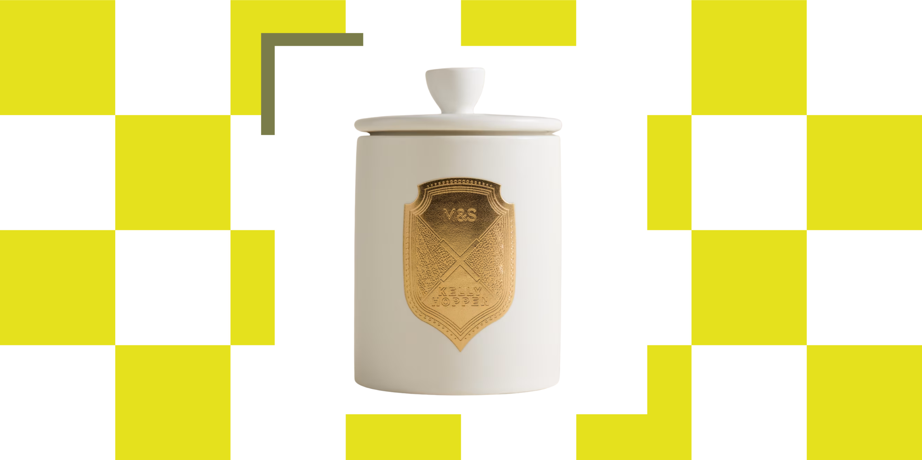 A scented candle in a white ceramic vessel with a matching lid and a gold crest in the middle on a neon yellow-green checkerboard background
