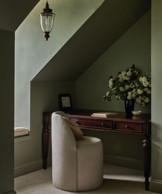 desk corned of room with curved upholstered chair and antique desk and green walls