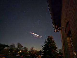 streaks of fire blaze the the night sky above a house.