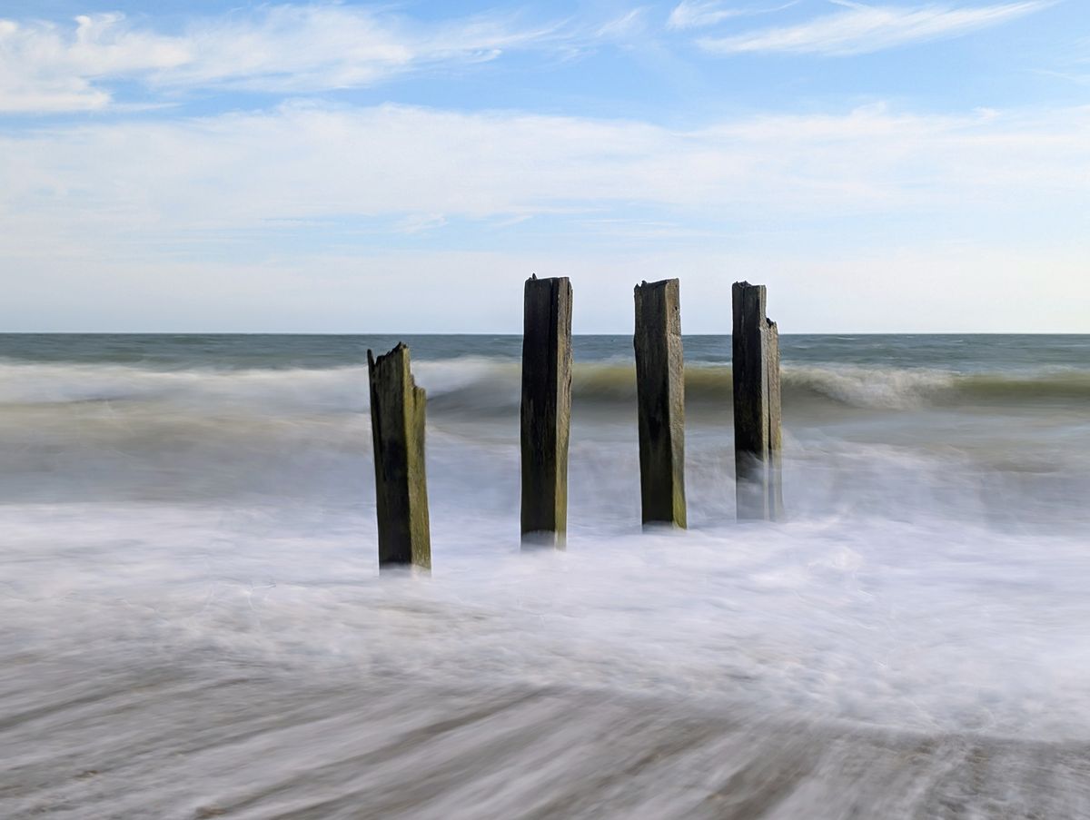 A damaged groyne on a UK beach, the high tide is smashing into it, with the moving water blurred using a long exposure photography technique