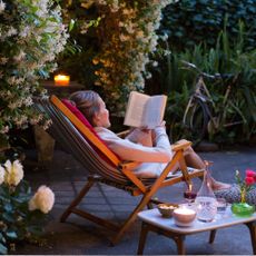 Woman relaxing on deck chair in back yard, reading a book with her cat watching 