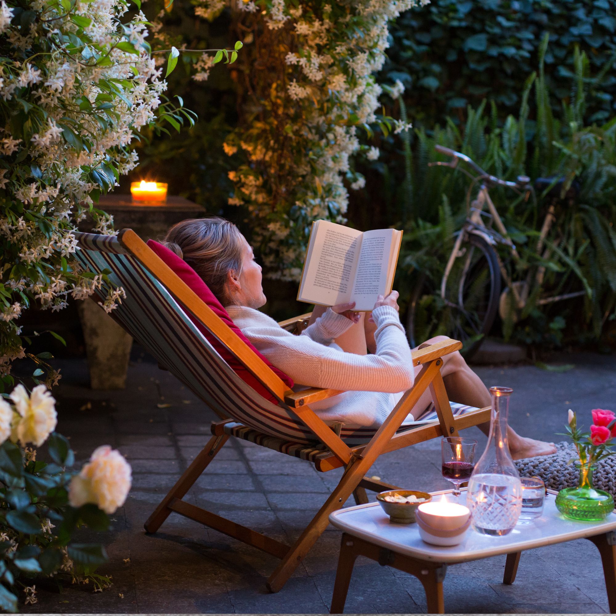 Woman relaxing on deck chair in back yard, reading a book with her cat watching 