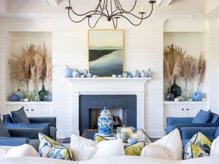 living room with blue painted pumpkins on mantel, pampas in colored glass vases in alcoves, blue armchairs, painting on mantel, coffee table with pumpkins