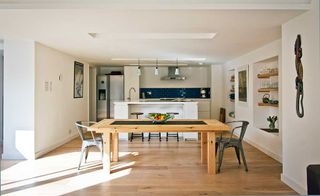 huge modern light kitchin and dining room in a garage conversion, with a large wooden dining table and white units, including a white island, and a wooden floor