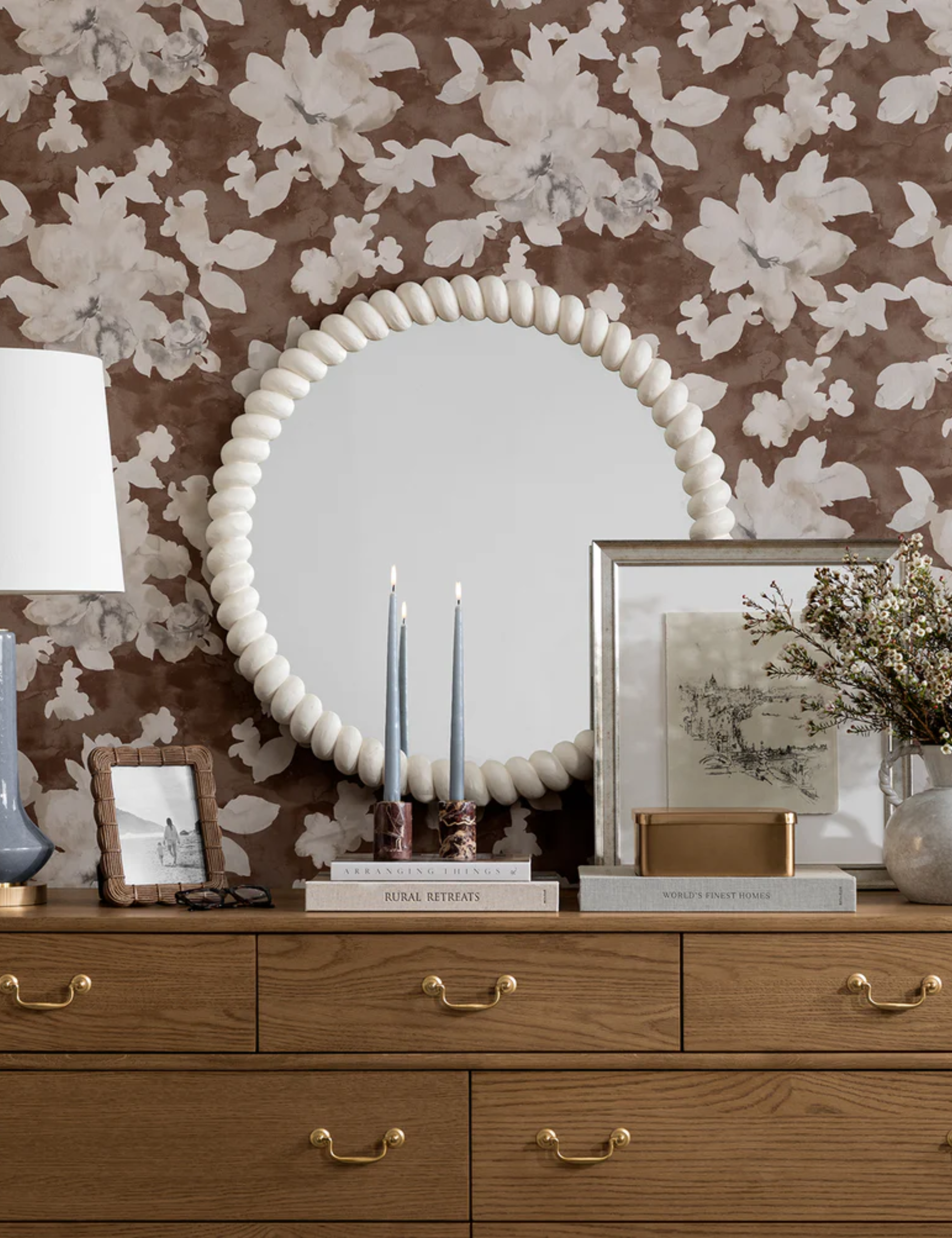 McGee & Co. Norina Mirror pictured against a bedroom wall that features a wooden dresser, floral wallpaper, and collected objects