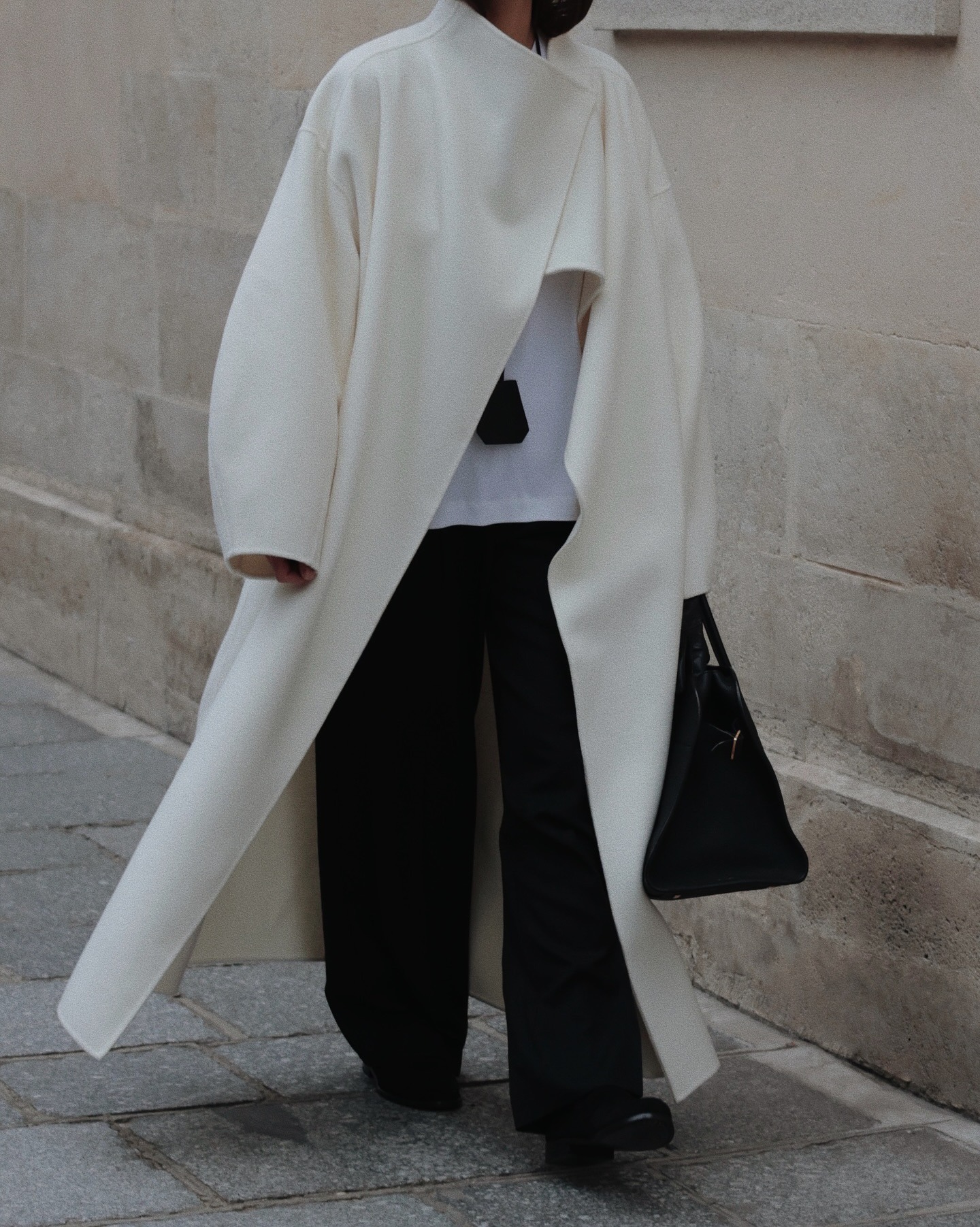 @modedamore wearing a long cream coat with black trousers and a black bag.