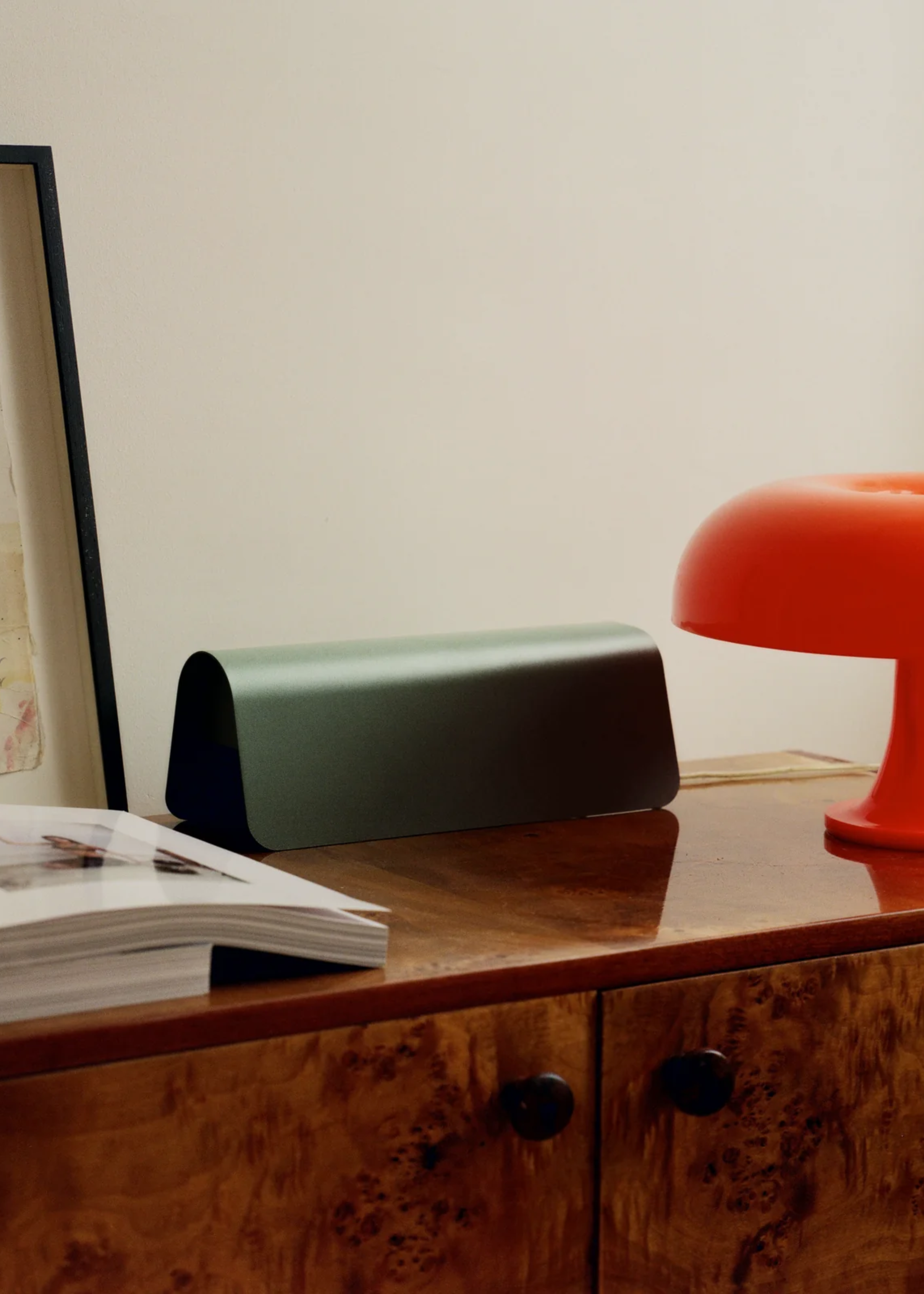 A green tented metal power strip cover on a wood sideboard by an orange lamp