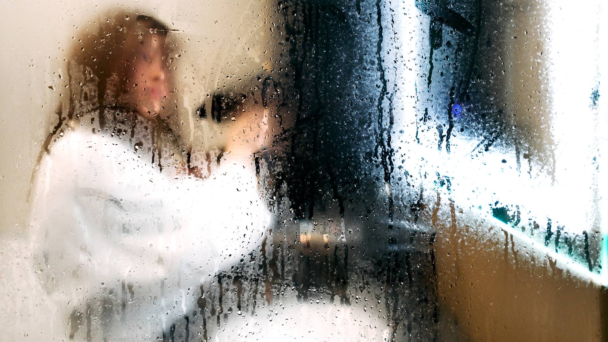 women in dressing gown drying hair seen in reflection of bathroom mirror covered in condensation