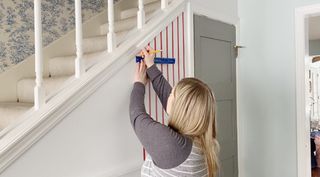 a woman marking up a white wall for stenciling, in an entryway