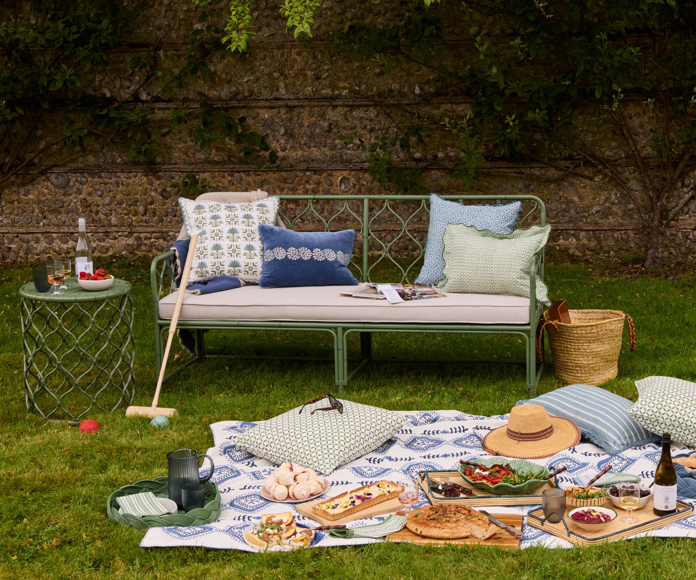 green garden sofa and side table styled with printed throw pillows with a picnic rug party spread styled on the floor