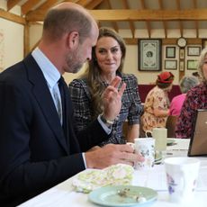 Prince William wearing a suit sitting with Princess Kate at a table full of cakes and tea