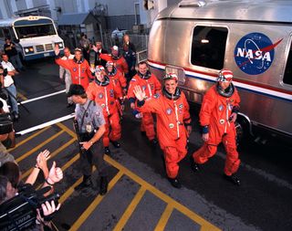 STS-86 crewmembers smile and wave as they prepare to board the astronaut van after departing from the Operations and Checkout Building at NASA's Kennedy Space Center in Florida, on Sept. 25, 1997. Leading the way are Pilot Michael Bloomfield (left) and Cmdr. James Wetherbee, followed by NASA astronauts David Wolf (left) and Wendy Lawrence (center), and Russian cosmonaut Vladimir Georgievich Titov. Behind them are NASA astronaut Scott Parazynski (left) and Jean-Loup Chretien of the French Space Agency, CNES. The seven-member crew is en route to Launch Pad 39A, where the space shuttle Atlantis awaits liftoff on a planned 10-day mission slated to be the seventh docking of a NASA space shuttle and the Russian Space Station Mir.