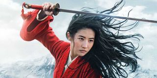 Mulan raises her sword above her head in a promotional picture from the 2020 live action adaptation.