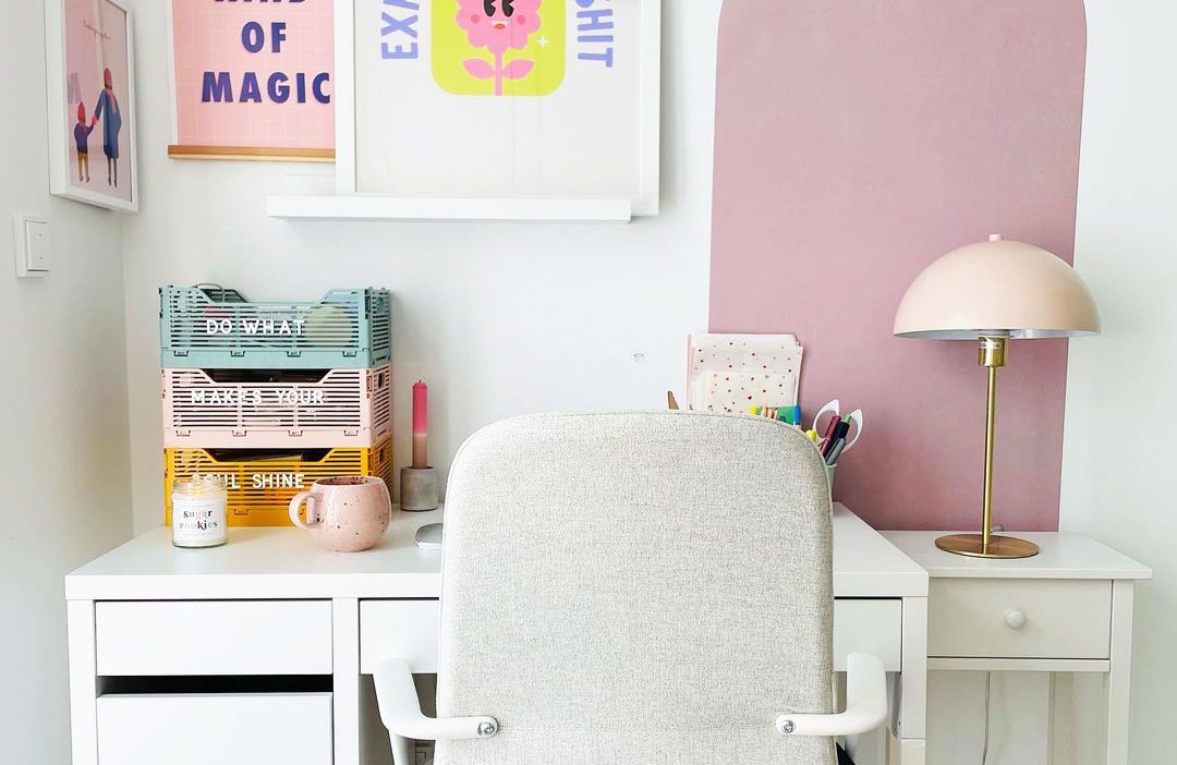 Bright WFH setup with colorful desk organizers, a white desk and chair in front of a pink color block wall