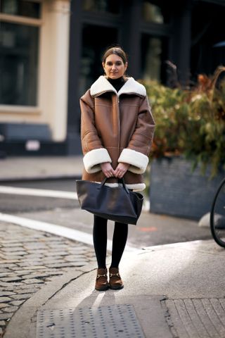 woman wearing shearling jacket, dress, tights, loafers, and tote bag