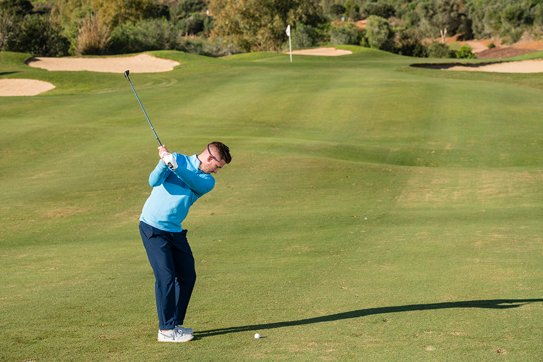 PGA Pro Alex Elliott demonstrating the position of hands at the top of the backswing, level with his trail shoulder, with the pin and the green in the distance