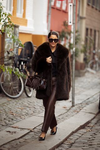 woman wearing brown faux fur coat, shirt, leather pants, bag, and heels