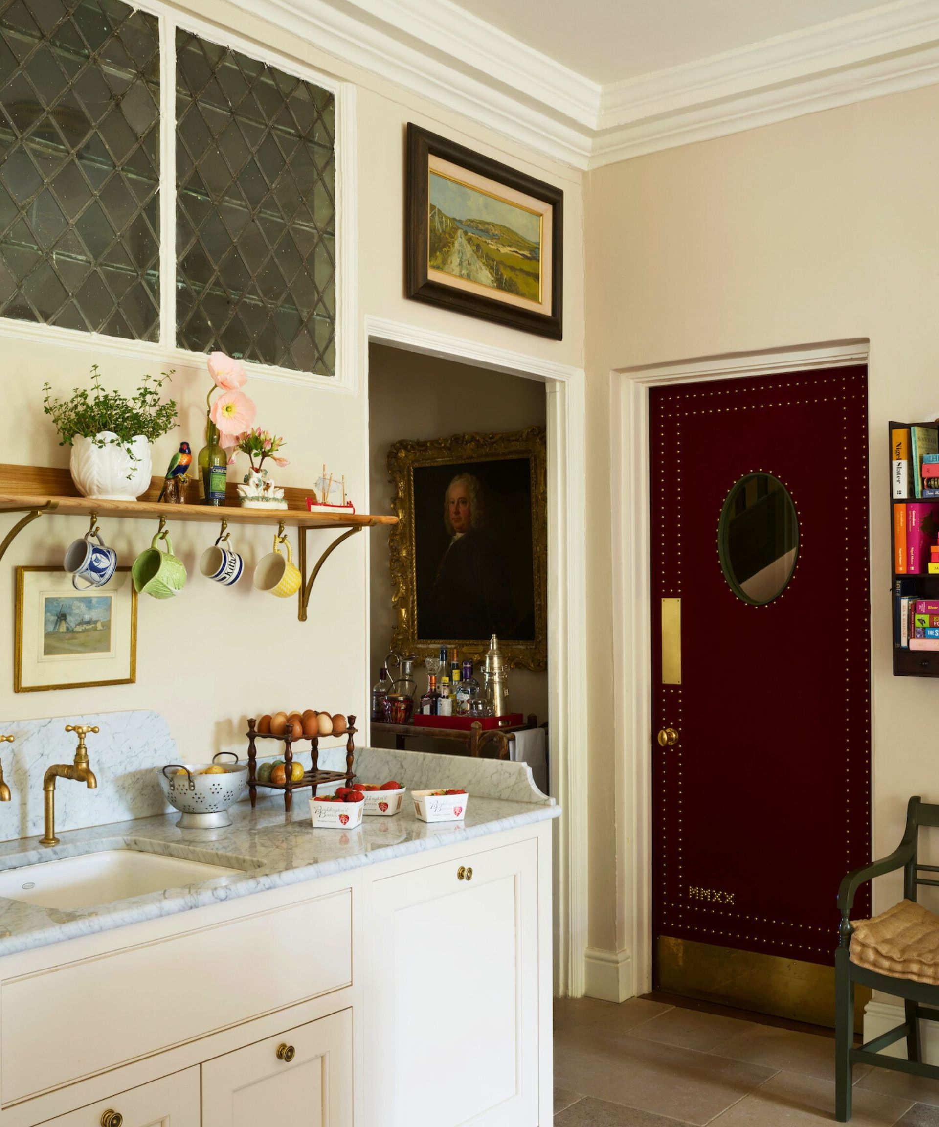 A cream kitchen with hanging mugs and a red door