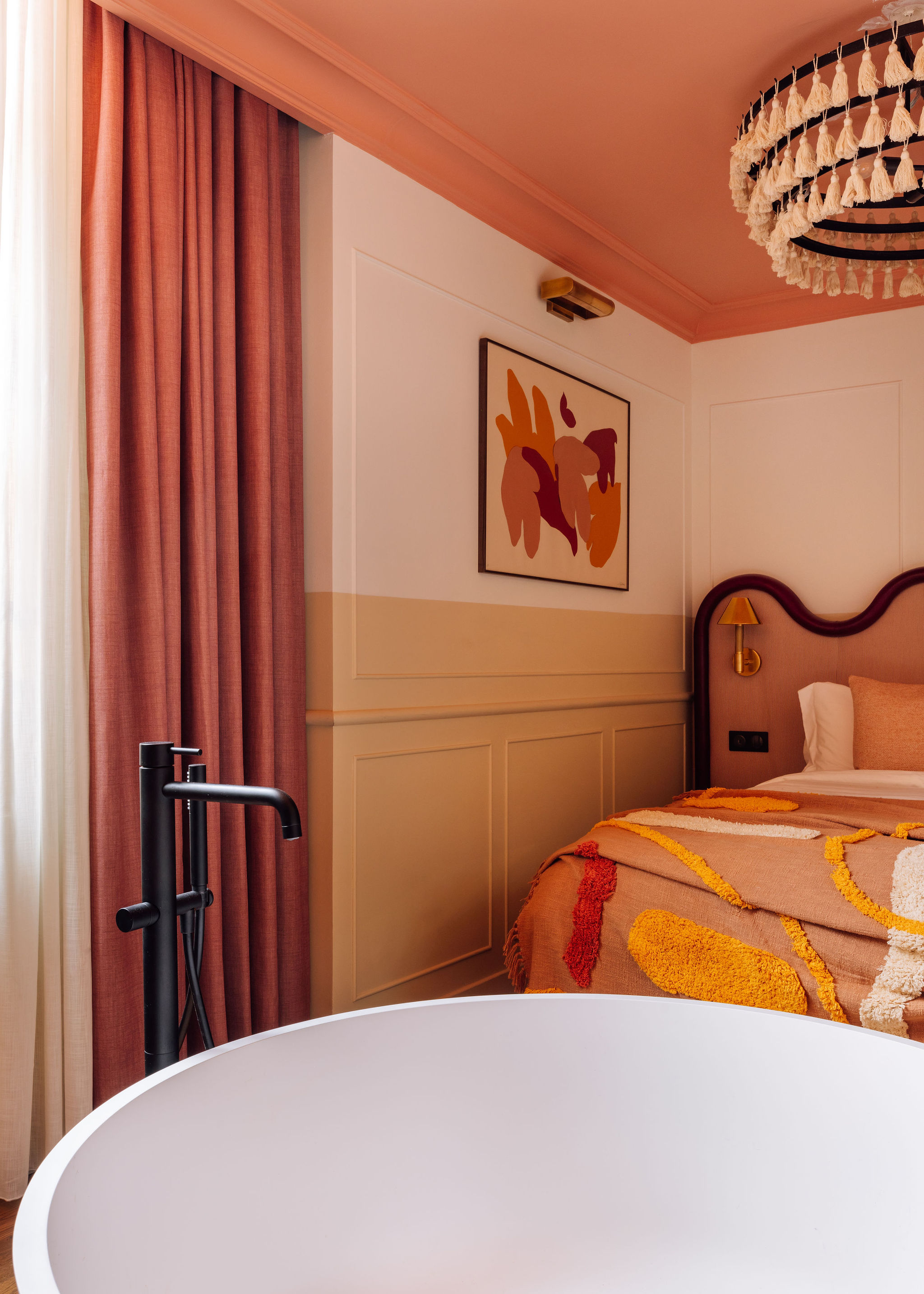 A vibrantly decorated hotel room boasts color-blocked walls n the tones of butter, orange, beige, and coral, sculptural furniture with a whimsical touch, and abstract artwork.
