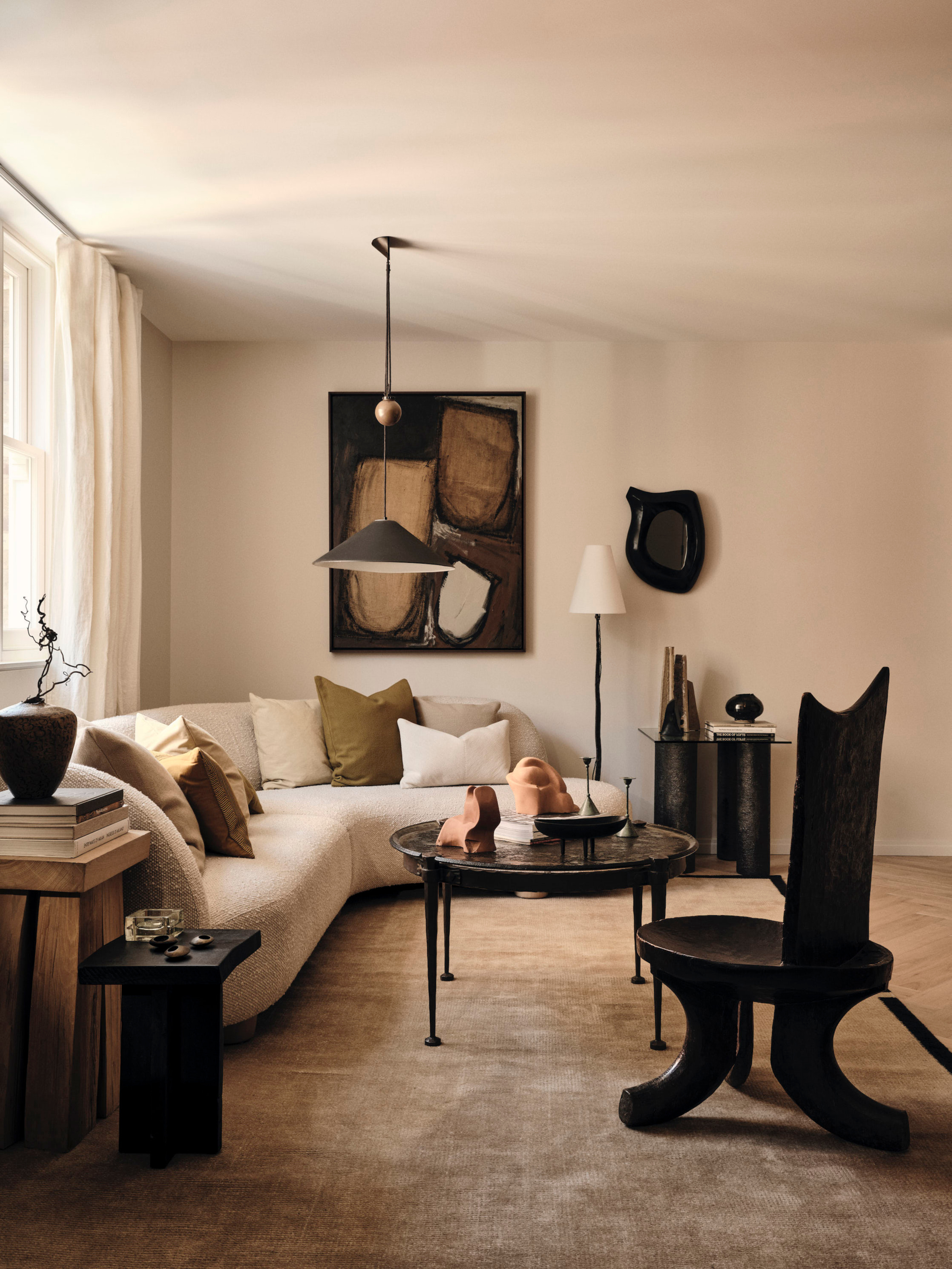 Beige living room with white curved corner sofa, black coffee table and armchair, brown abstract art and black pendant light