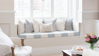 White living room with window seat and shutters on the windows to show an idea for how to improve the air quality of your home by opening windows