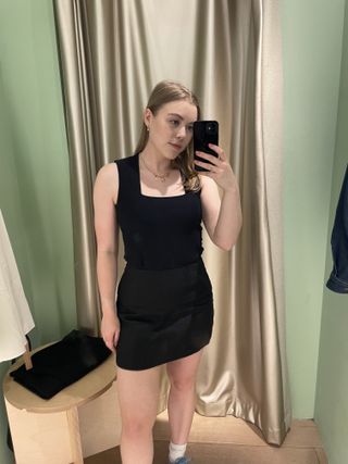Woman in dressing room wears black tank top, black linen skirt